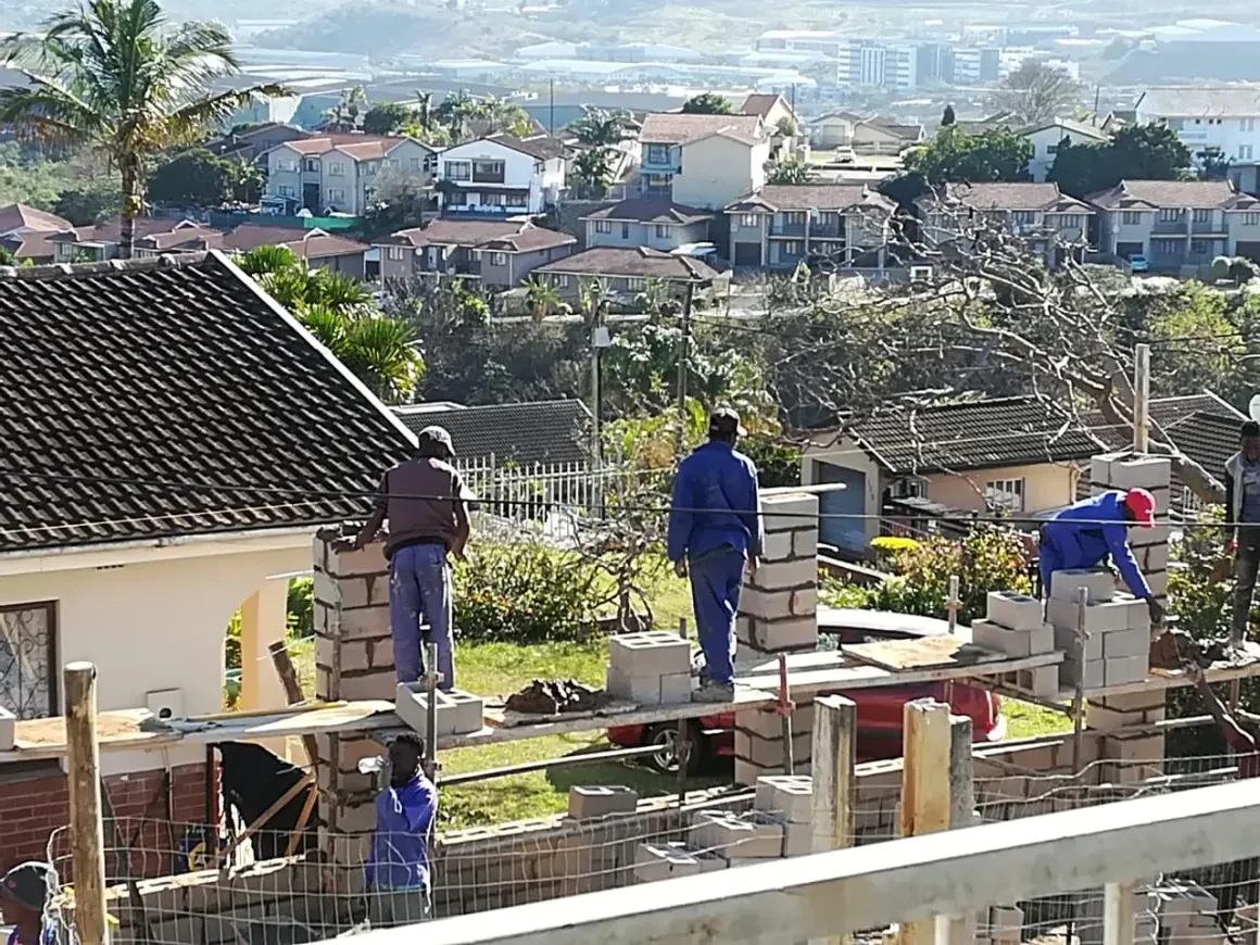 Project site — workers laying bricks on perimeter wall
