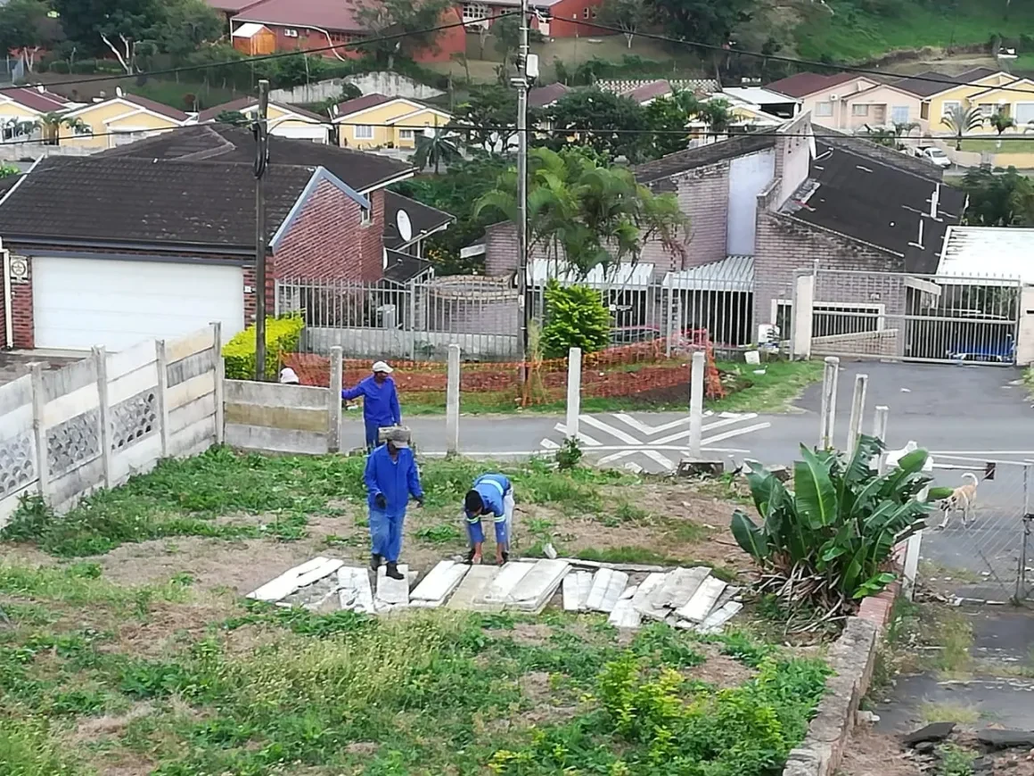 Project site — workers on cleared land with neighbourhood view