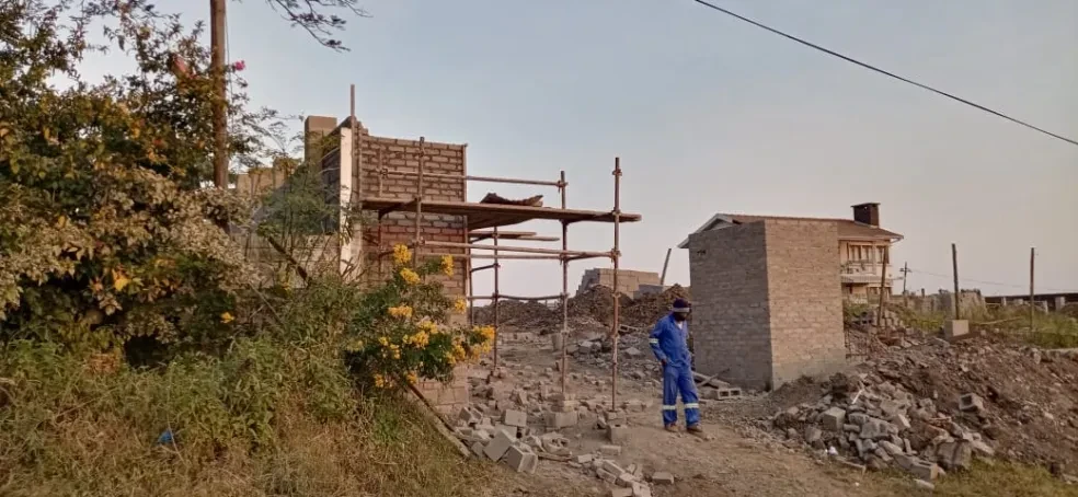 Project site — brick building with scaffolding and worker in blue overalls at dusk
