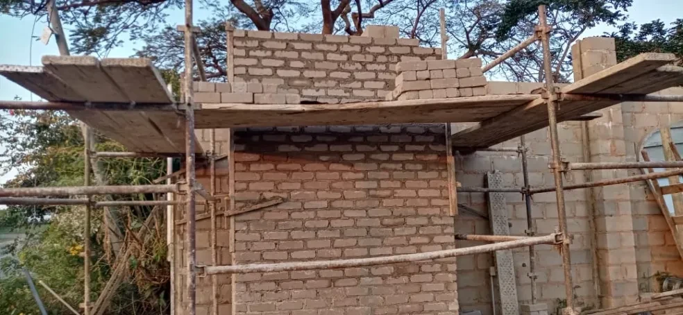 Project site — brick building rising with scaffolding and worker at dusk
