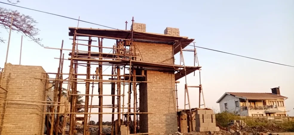Project site — brick wall under construction with wooden scaffolding and trees