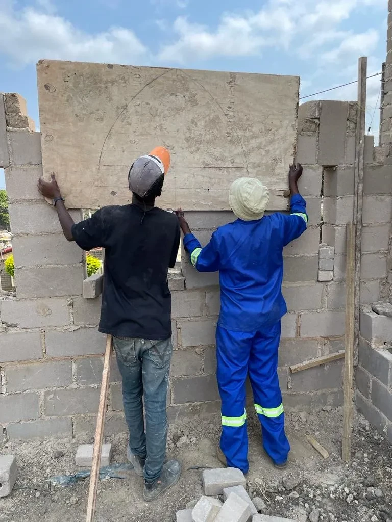 Project site — two workers lifting concrete panel onto block wall