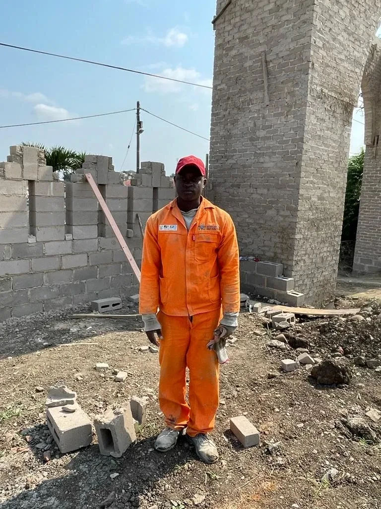 Project site — construction worker in orange overalls beside brick arch
