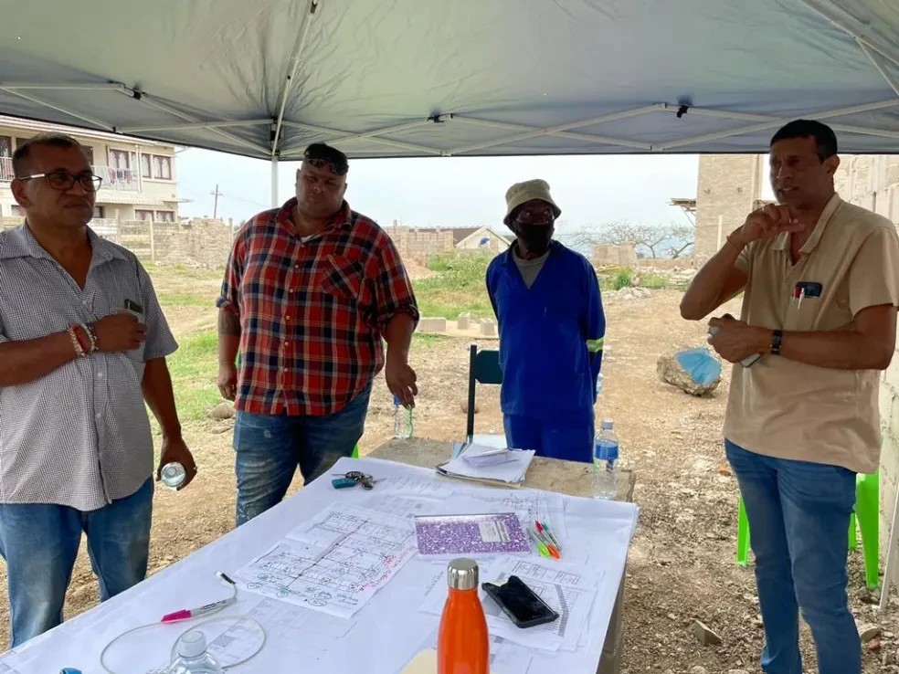 Project site — four people reviewing architectural plans under site tent