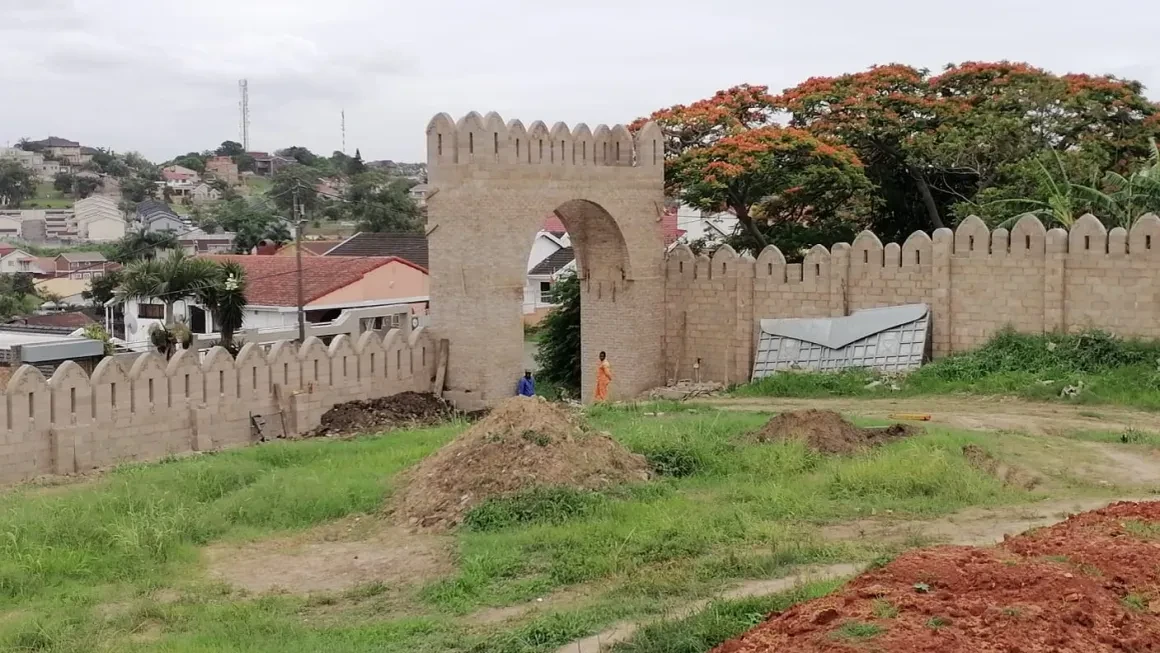 Project site — fortified white building with crenellated parapet and worker on scaffolding