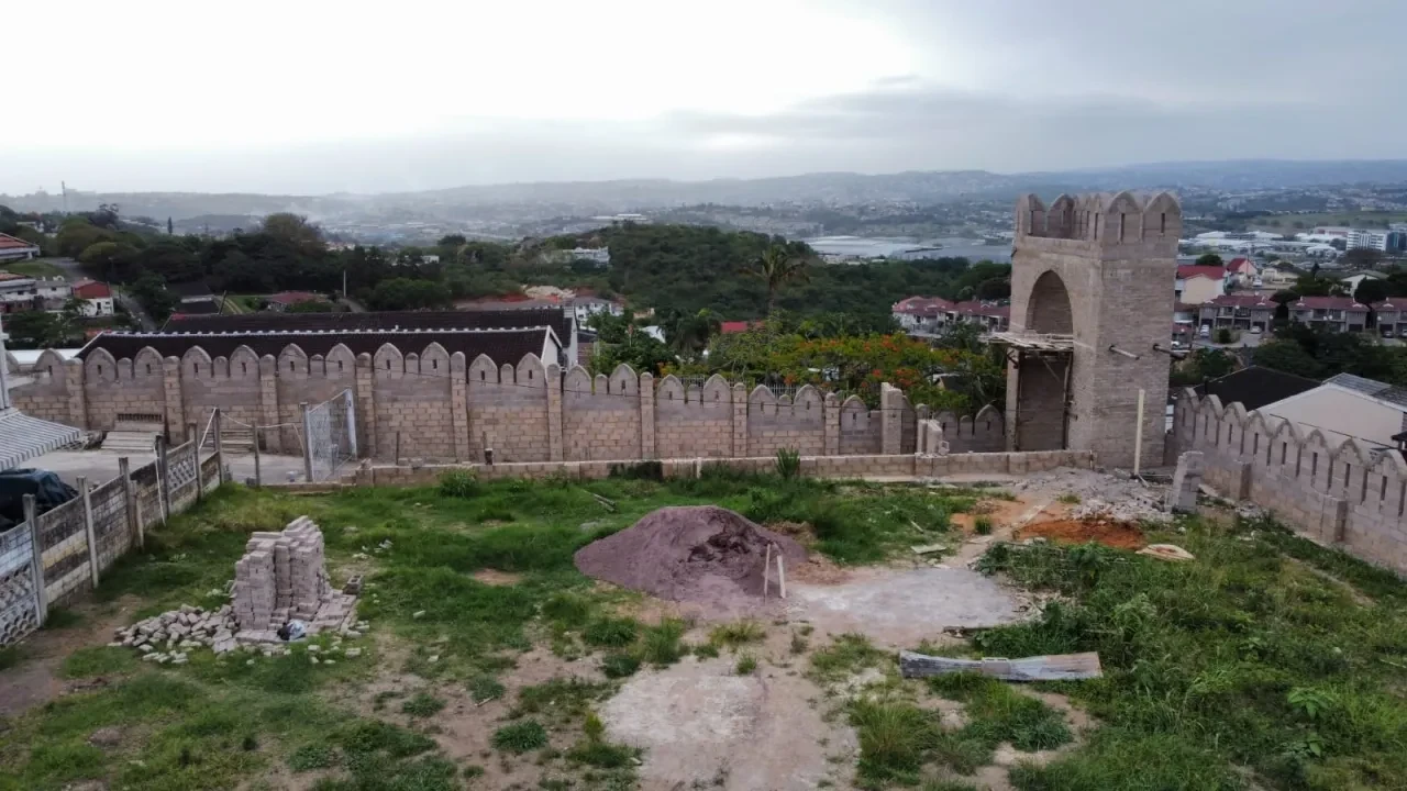 Project site — crenellated gateway tower with arched entrance and Durban suburban backdrop