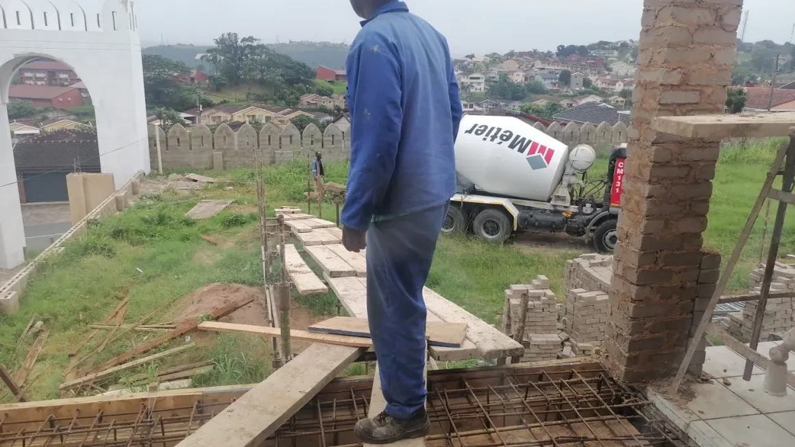 Project site — worker on scaffolding with Metier cement mixer truck and crenellated wall